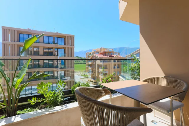 Balkon ze stolikiem i fotelami, w tle zieleń i góry